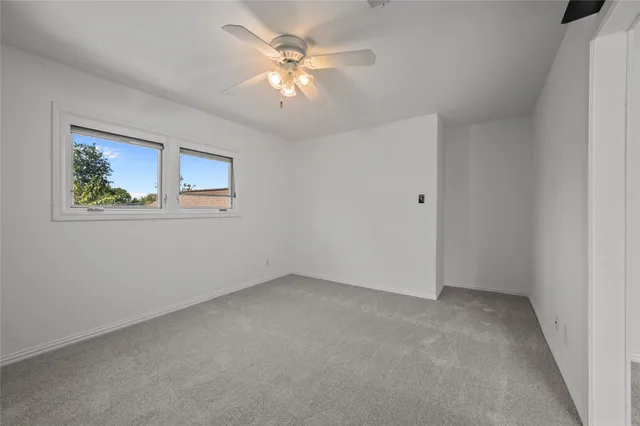 a view of an empty room with wooden floor and fan