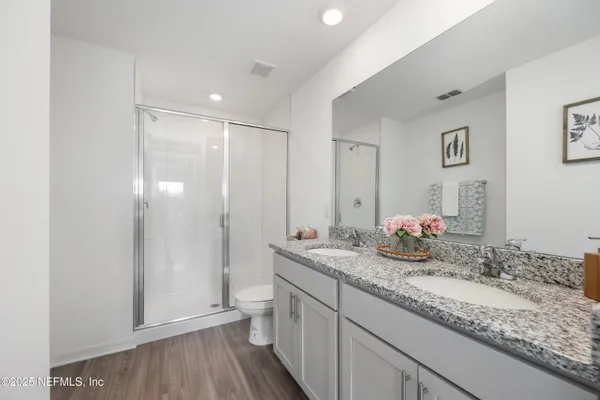 a bathroom with a granite countertop double vanity sink mirror and shower