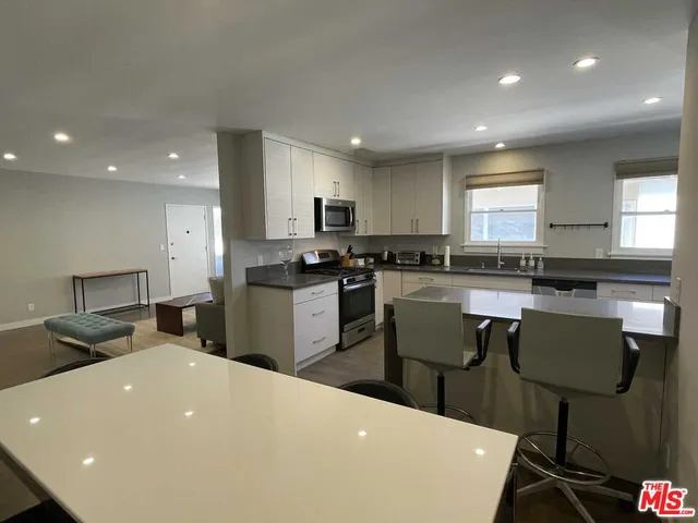 a living room with stainless steel appliances a dining table wooden floor windows and a kitchen view