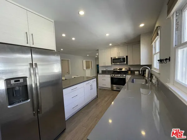 a kitchen with stainless steel appliances granite countertop a refrigerator a sink a stove and a refrigerator with wooden floor