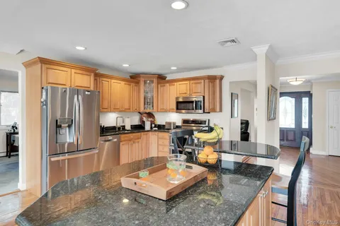 a kitchen with stainless steel appliances granite countertop a refrigerator a stove a sink a dining table and chairs with wooden floor