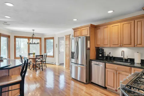 a kitchen with stainless steel appliances granite countertop a stove top oven a refrigerator a dining table and chairs with wooden floor