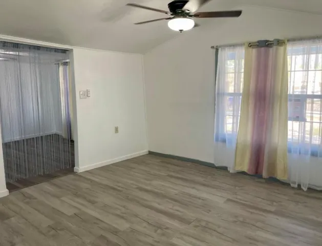 an empty room with wooden floor fan and windows