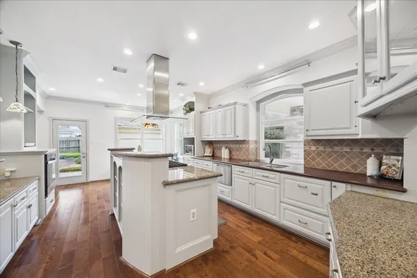 a kitchen with stainless steel appliances kitchen island granite countertop a stove a sink and white cabinets with wooden floor