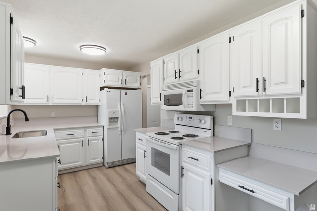 629 King Circle Layton, UT 84041 - Photo 5 of 26 Kitchen featuring white cabinetry with black hardware, light-colored countertops, stainless steel sink with a black gooseneck faucet, white appliances including a range and microwave, and wood-finish flooring