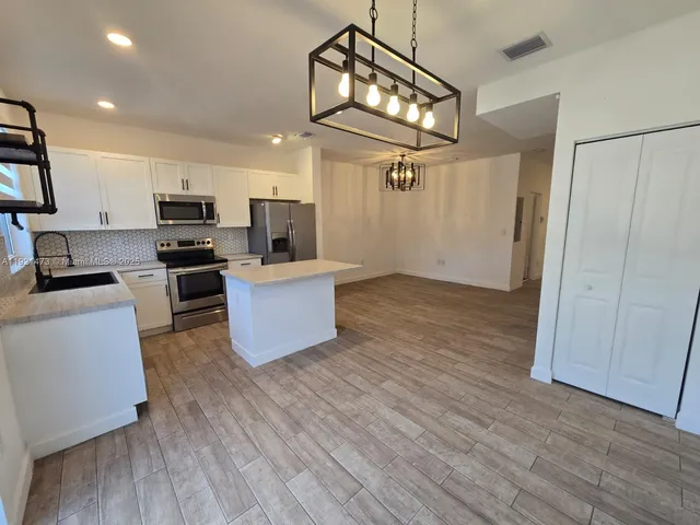 a kitchen with stainless steel appliances kitchen island a wooden floor and white cabinets