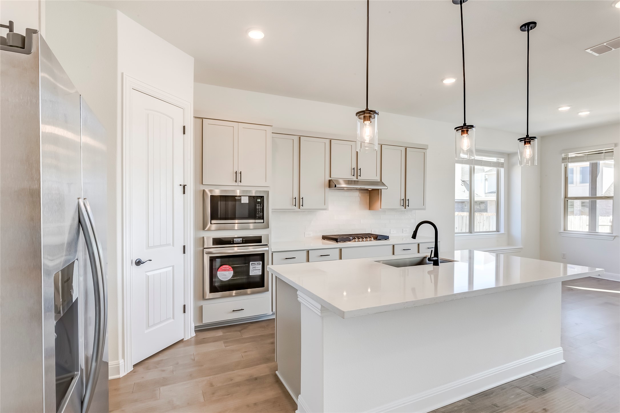 920 Old Gdn Road Leander, TX 78641 - Photo 12 of 39 Kitchen with appliances with stainless steel finishes, decorative light fixtures, an island with sink, light wood-style flooring, and light stone countertops