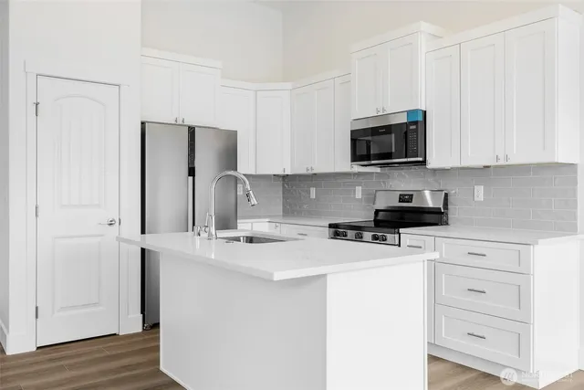 a kitchen with stainless steel appliances granite countertop a refrigerator stove a sink and white cabinets with wooden floor