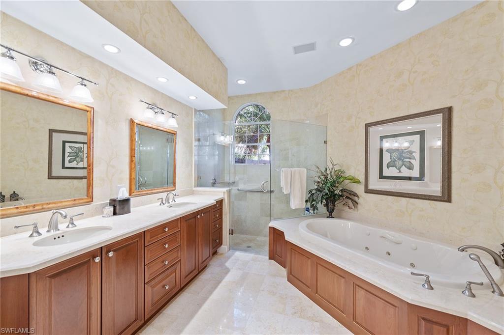 8063 Vizcaya Way Naples, FL 34108 - Photo 12 of 28 a spacious bathroom with a double vanity sink a large mirror a bathtub and shower