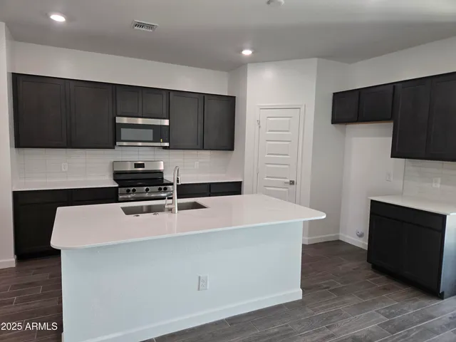 a kitchen with stainless steel appliances granite countertop a sink a stove a refrigerator cabinets and chairs