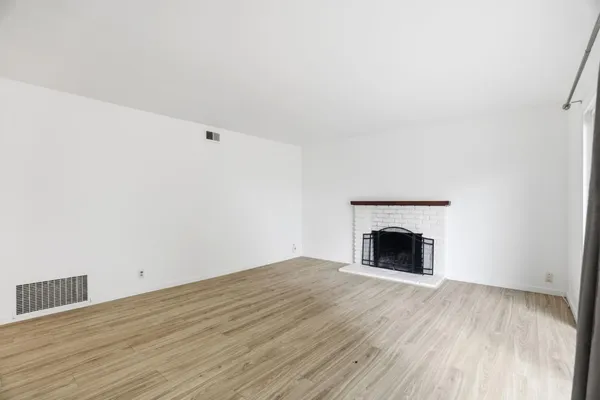 a view of an empty room with wooden floor and a fireplace