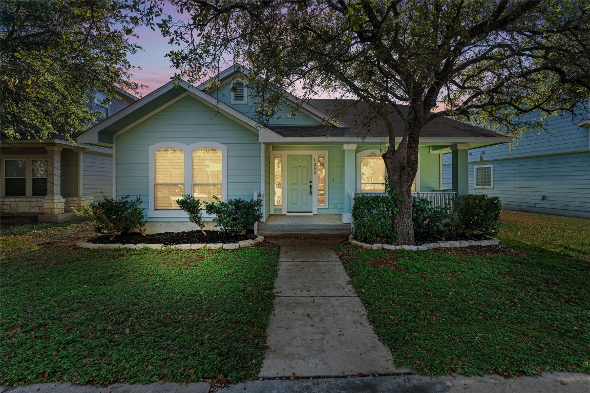 Craftsman-style house with a beautifully landscaped front lawn and covered porch, nestled under a canopy of mature trees.