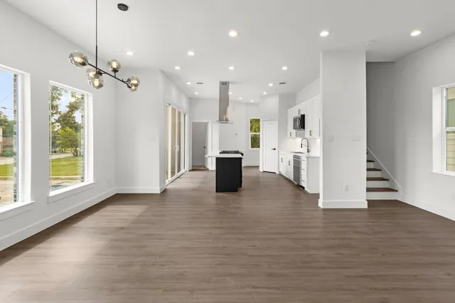 a view of an empty room and kitchen with wooden floor and windows