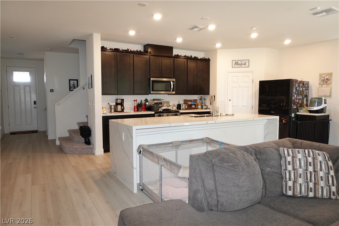 6959 Rancho Pk Court Las Vegas, NV 89113 - Photo 8 of 8 Kitchen featuring an island with sink, light wood finished floors, light stone countertops, open floor plan, and dark wood finish cabinets