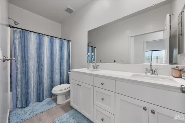 a bathroom with double sink a toilet a mirror and shower