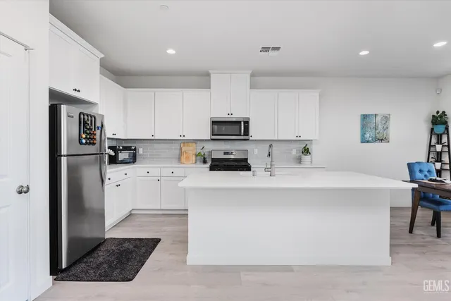 a kitchen with stainless steel appliances a refrigerator sink stove and white cabinets