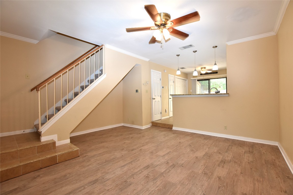a view of an empty room with wooden floor and a ceiling fan