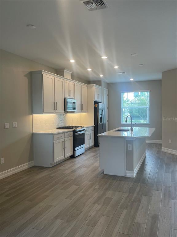 4596 Almada Lane Wesley Chapel, FL 33543 - Photo 2 of 56 a large kitchen with stainless steel appliances a large counter top a stove and a wooden floors