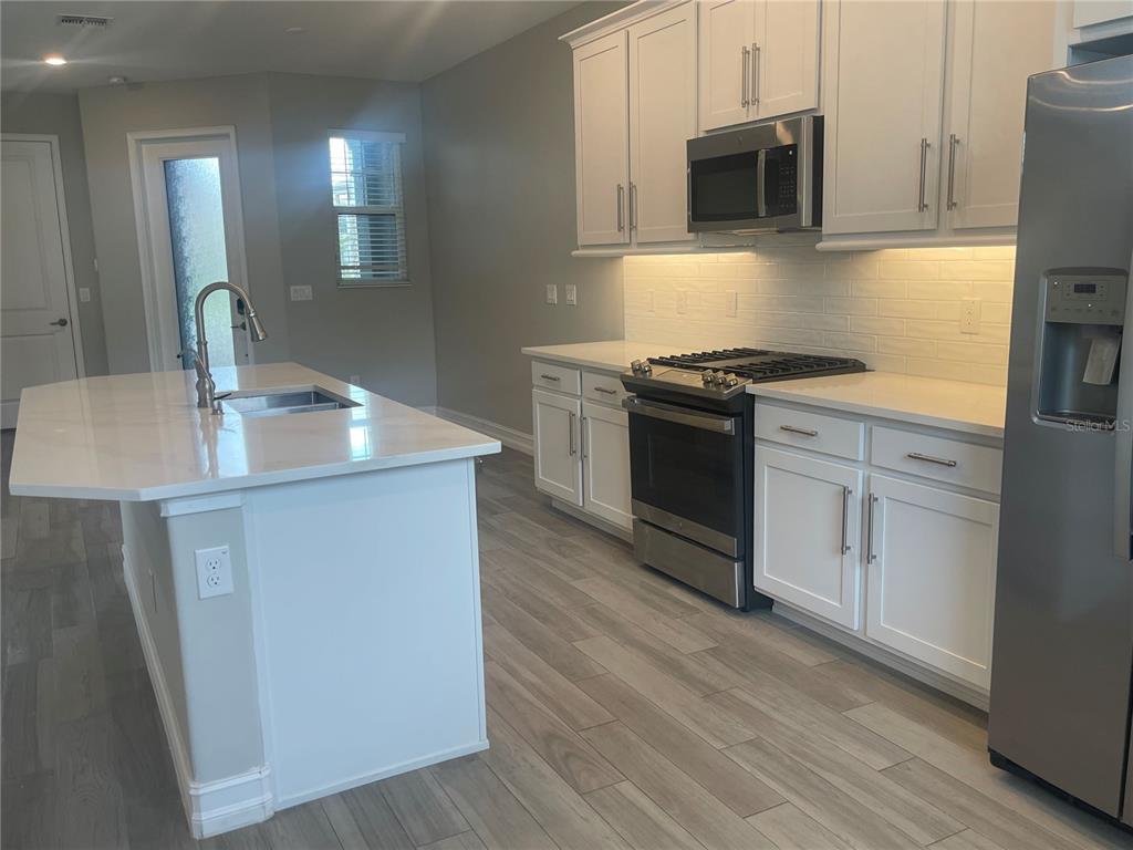 4596 Almada Lane Wesley Chapel, FL 33543 - Photo 6 of 56 a kitchen with stainless steel appliances white cabinets a sink a stove a microwave and wooden floors