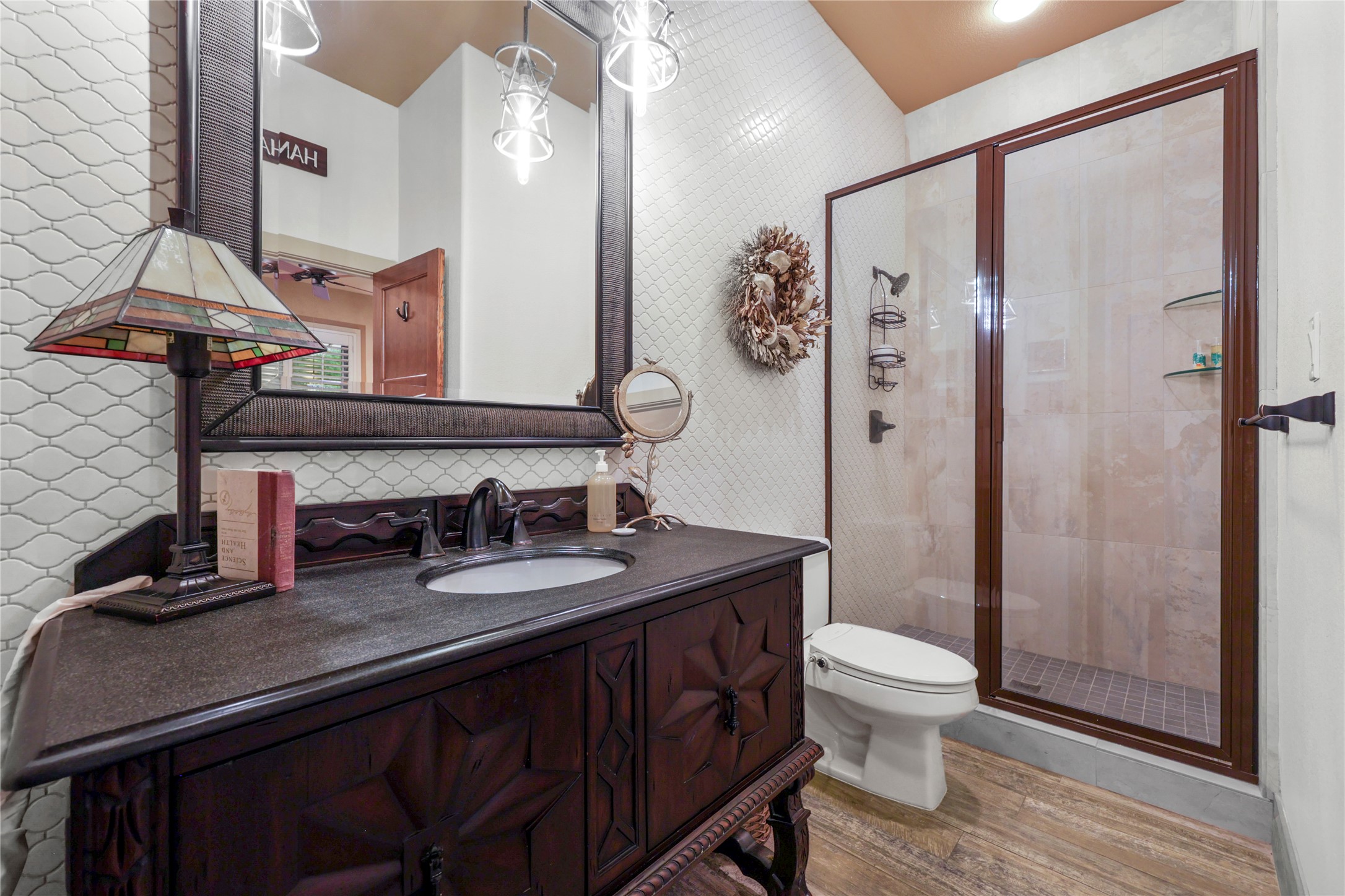 17501 Navigation Lane Lago Vista, TX 78645 - Photo 29 of 40 Downstairs guest bathroom featuring a dark wood vanity with an integrated sink, a glass-enclosed shower, and wave-patterned wall tiling