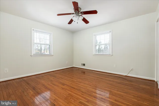 an empty room with wooden floor ceiling fan and windows