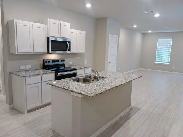 a kitchen with stainless steel appliances granite countertop a sink a stove a microwave a sink and white cabinets