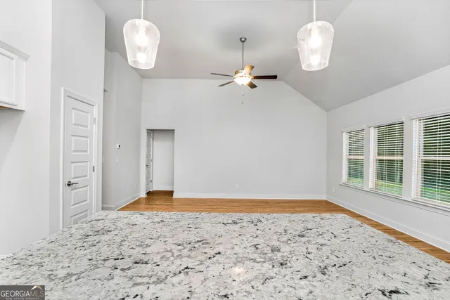 a view of an empty room with a kitchen and ceiling fan