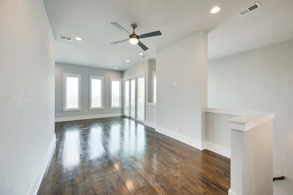 an empty room with wooden floor ceiling fan and windows
