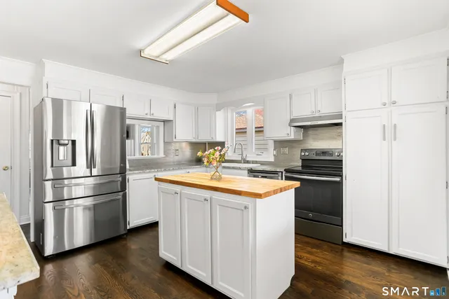 a kitchen with stainless steel appliances granite countertop a refrigerator a stove a sink and white cabinets with wooden floor