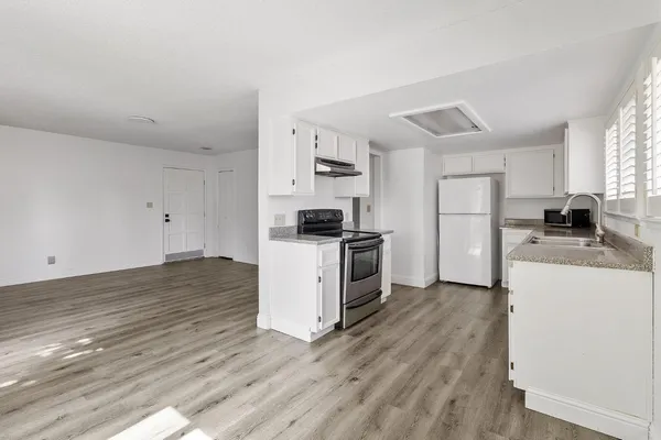 a kitchen with granite countertop a stove top oven a sink a refrigerator and white cabinets with wooden floor