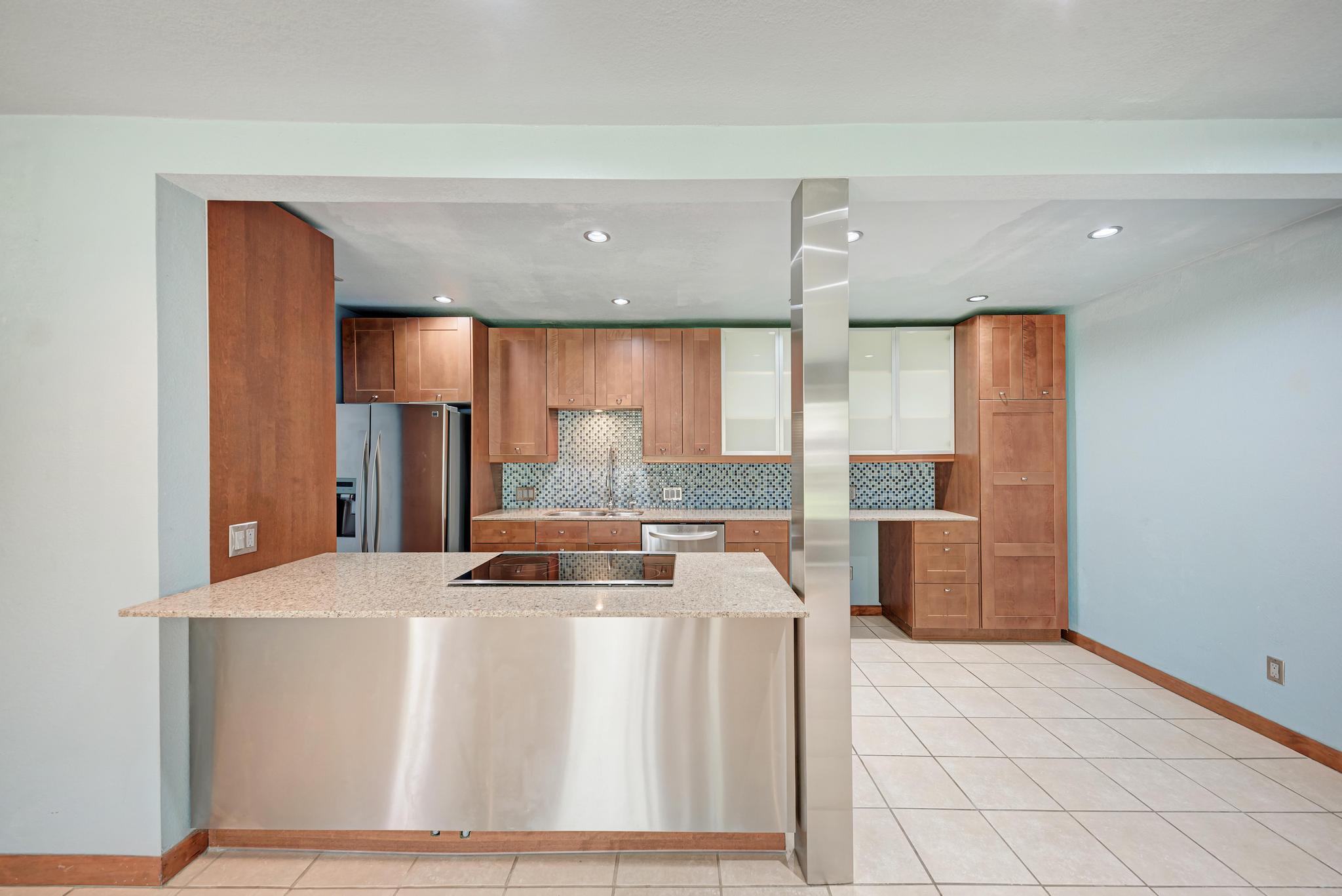 8210 Bent Tree Road, Unit 138 Austin, TX 78759 - Photo 14 of 23 Kitchen with a peninsula, wood finish cabinets, decorative backsplash, stainless steel appliances, and light stone countertops