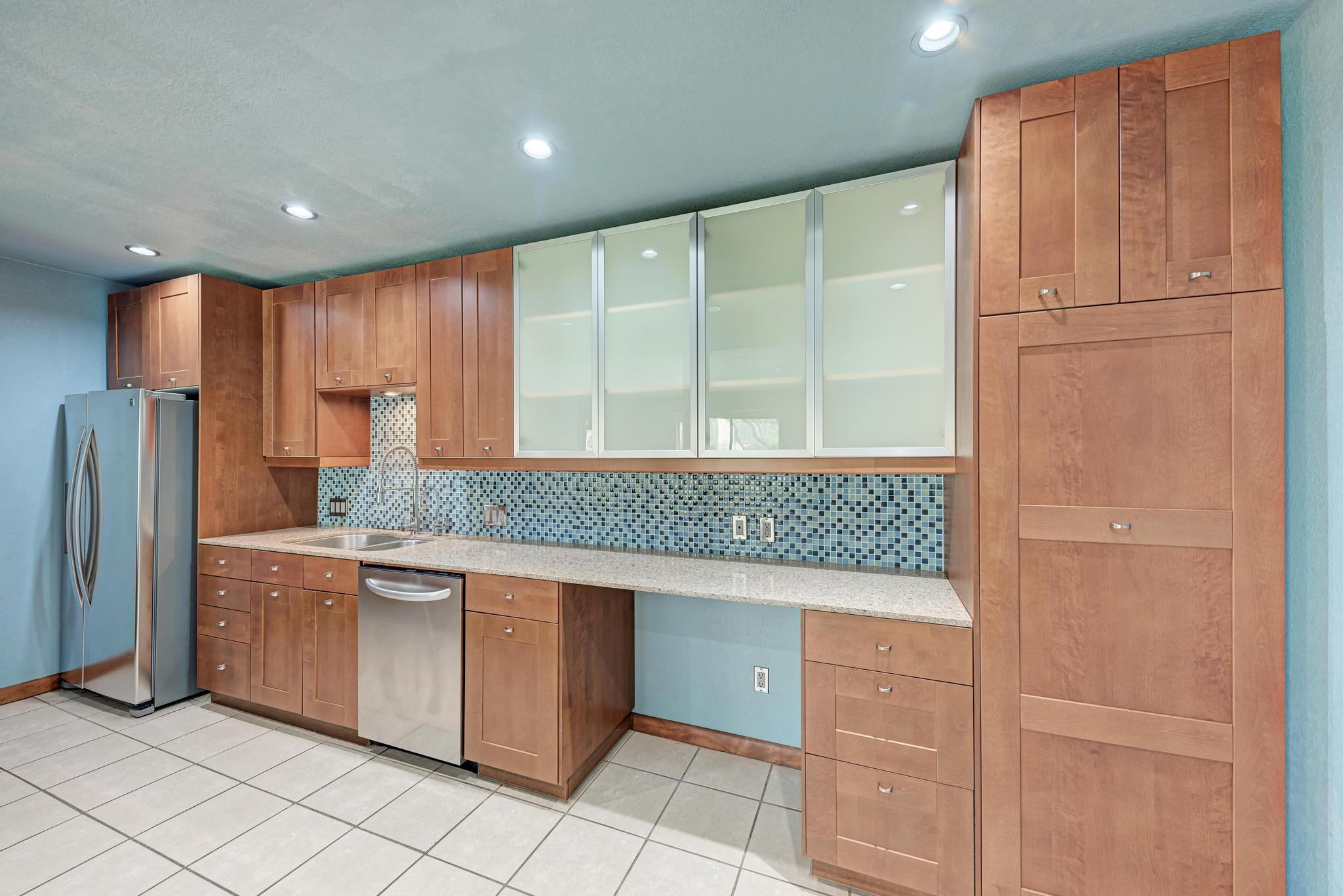 8210 Bent Tree Road, Unit 138 Austin, TX 78759 - Photo 15 of 23 Kitchen featuring glass insert cabinets, stainless steel appliances, wood finish cabinets, light stone counters, and backsplash