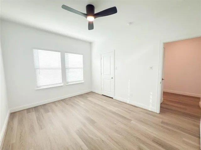 an empty room with wooden floor ceiling fan and windows