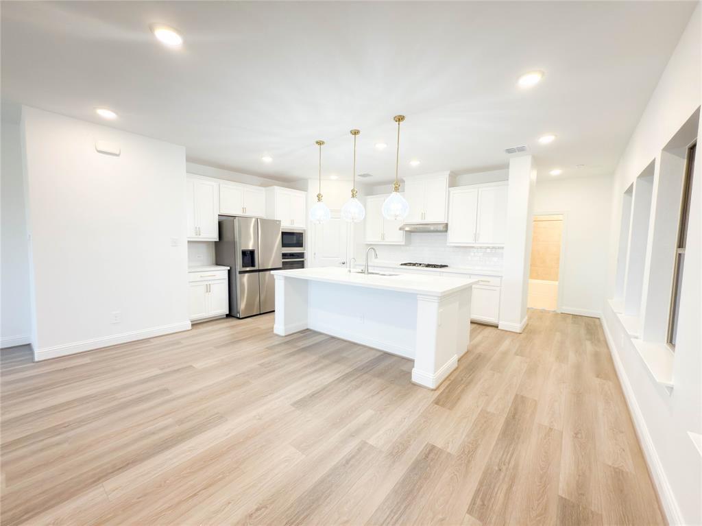 114 Settlers Way Euless, TX 76040 - Photo 5 of 38 a large white kitchen with kitchen island a sink a stove a refrigerator and white cabinets with wooden floor