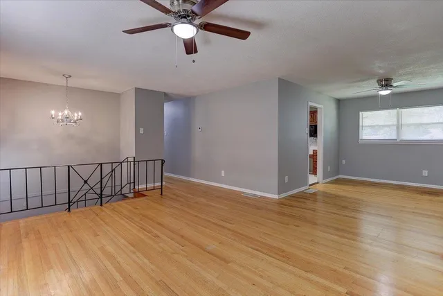 an empty room with wooden floor fan and windows