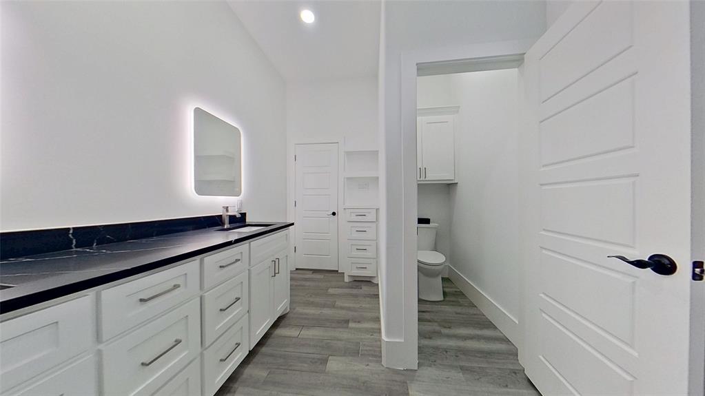 3248 North Cardinal Road Azle, TX 76020 - Photo 24 of 29 Spacious bathroom featuring a dual vanity with white cabinetry and dark countertops, an illuminated mirror, and wood-finish flooring