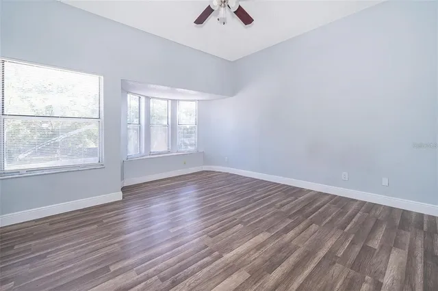 an empty room with wooden floor chandelier fan and windows