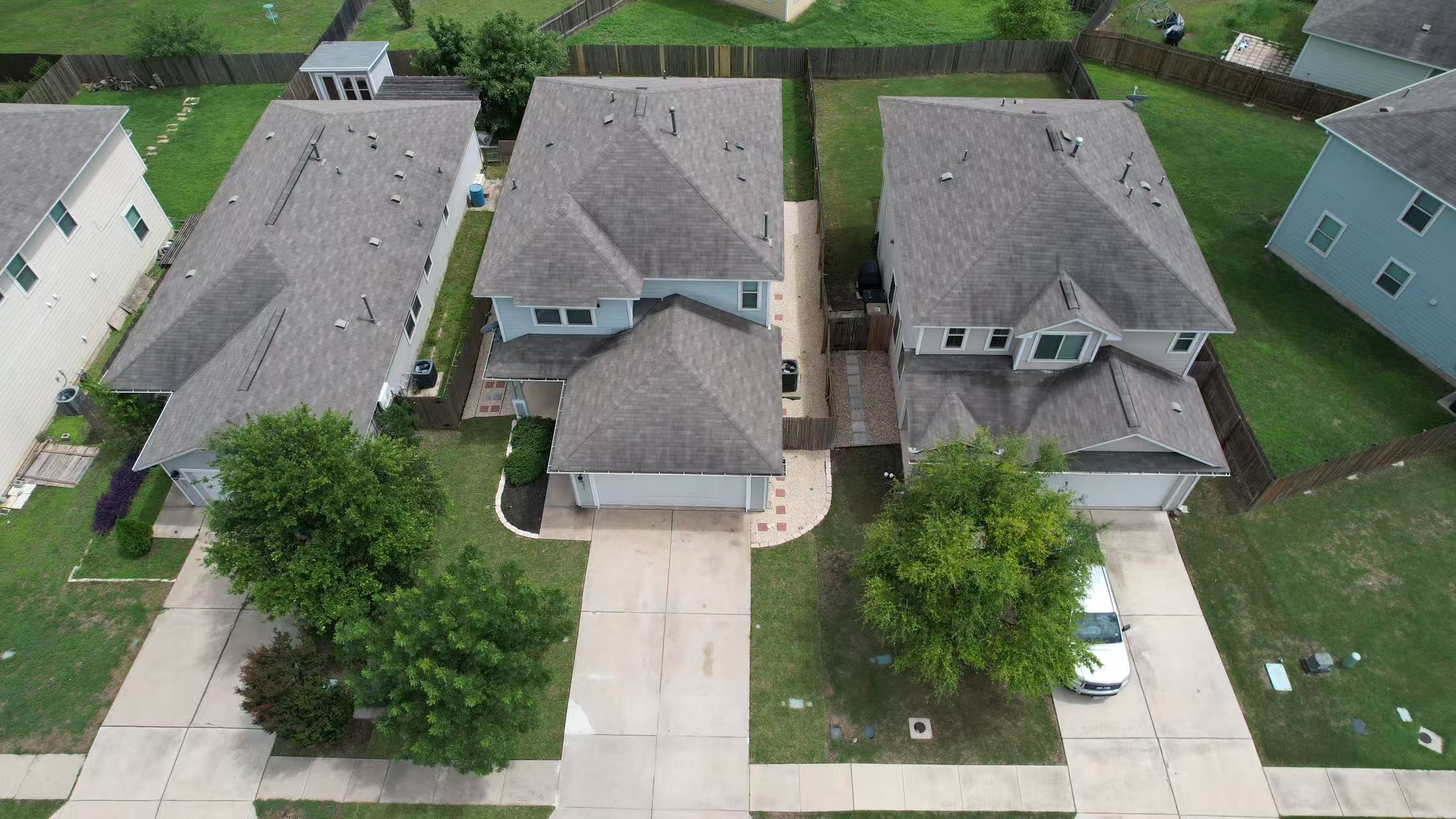 251 Triumph Road Buda, TX 78610 - Photo 2 of 26 An aerial perspective reveals three inviting suburban homes, each with its own concrete driveway and well-kept lawn.