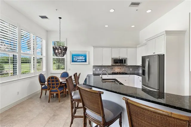 a kitchen with stainless steel appliances granite countertop a sink a stove a refrigerator cabinets and chairs