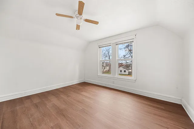 an empty room with wooden floor ceiling fan and windows