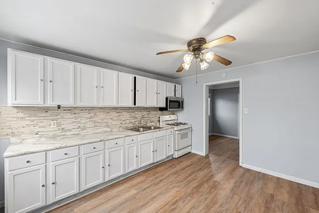 a kitchen with granite countertop a stove a sink and dishwasher with white cabinets