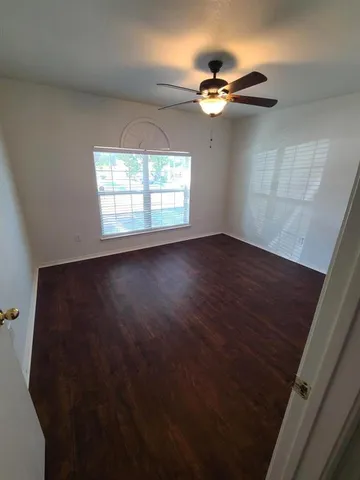 an empty room with wooden floor fan and windows