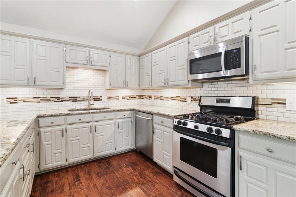 8463 Crestview Road Sanger, TX 76266 - Photo 7 of 36 Kitchen featuring vaulted ceiling, stainless steel appliances, dark wood-style flooring, light stone counters, and tasteful backsplash