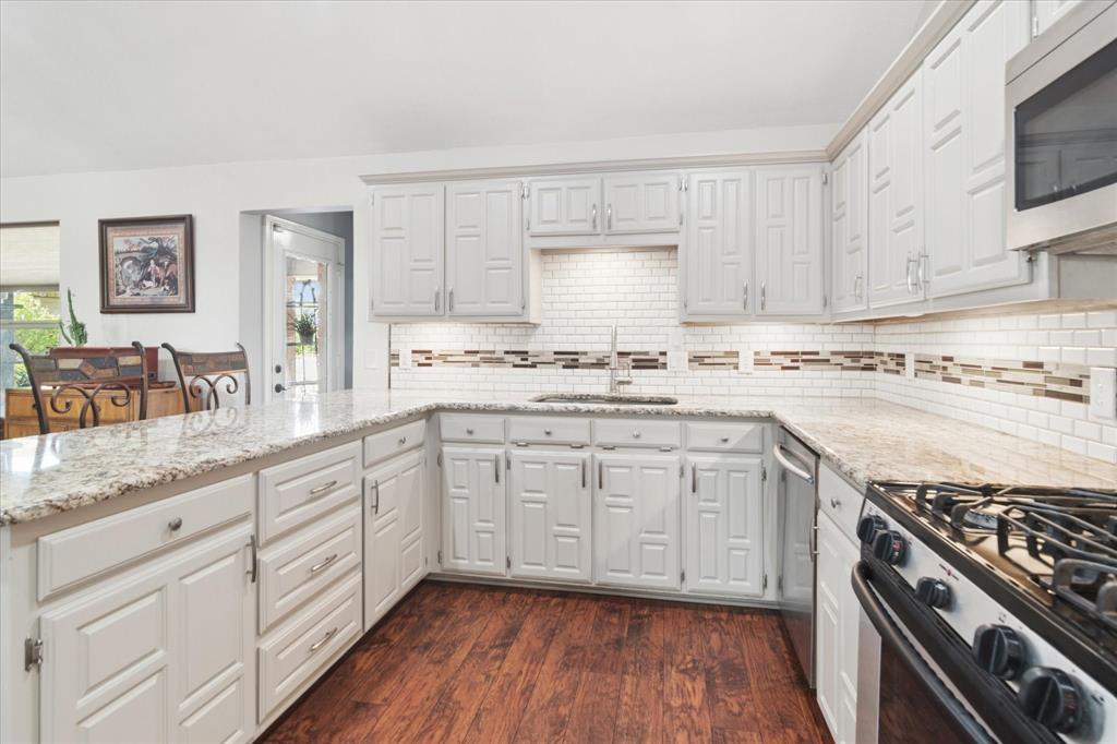 8463 Crestview Road Sanger, TX 76266 - Photo 8 of 36 Kitchen with stainless steel appliances, light stone counters, dark wood-style flooring, a peninsula, and backsplash