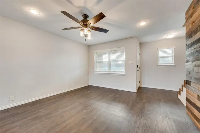 an empty room with wooden floor fan and windows