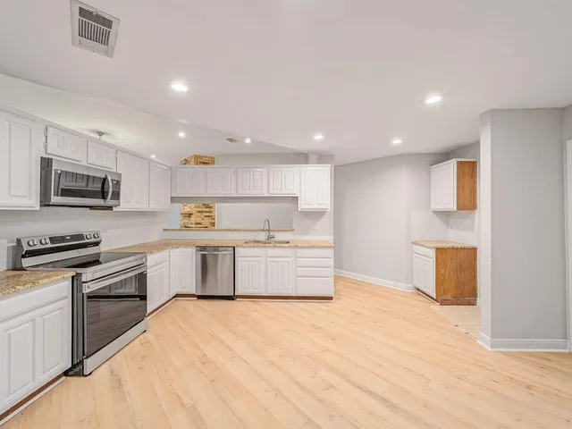 a kitchen with stainless steel appliances granite countertop a stove top oven a sink dishwasher and a refrigerator with wooden floor