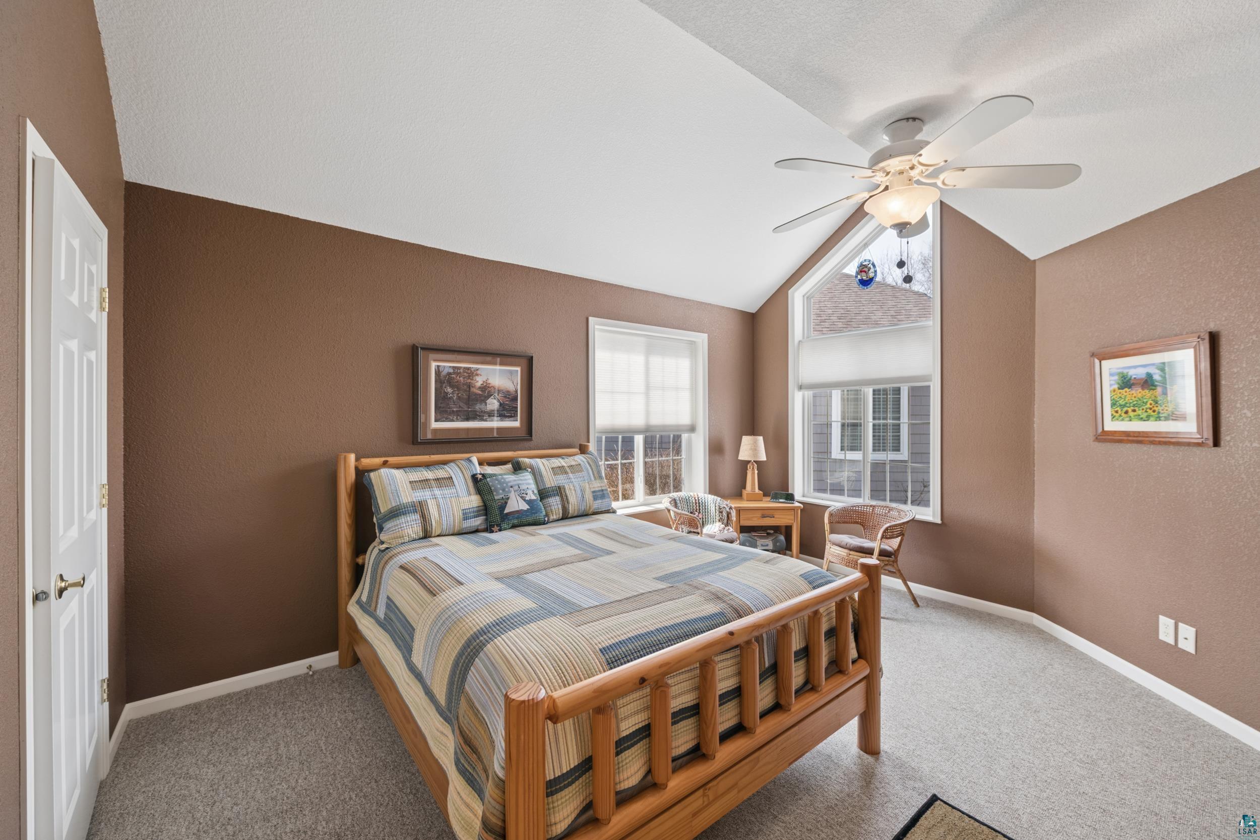 34590 Bay View Road, Unit 801 Bayfield, WI 54814 - Photo 13 of 36 Vaulted ceiling bedroom featuring a ceiling fan with integrated lighting, a large triangular window, two rectangular windows with blinds, and light-toned carpet flooring