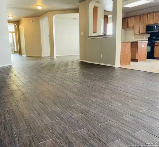 a view of an empty room with wooden floor and a kitchen