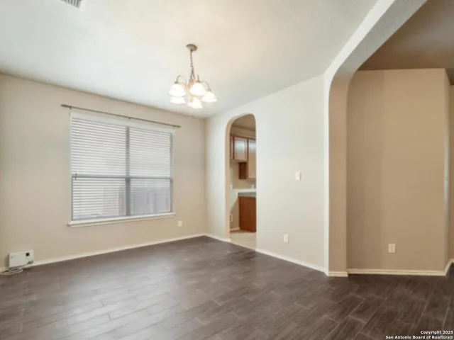 an empty room with wooden floor chandelier and windows