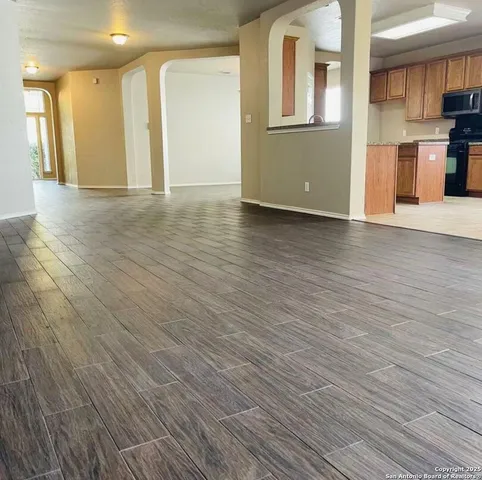 a view of an empty room with wooden floor and a kitchen